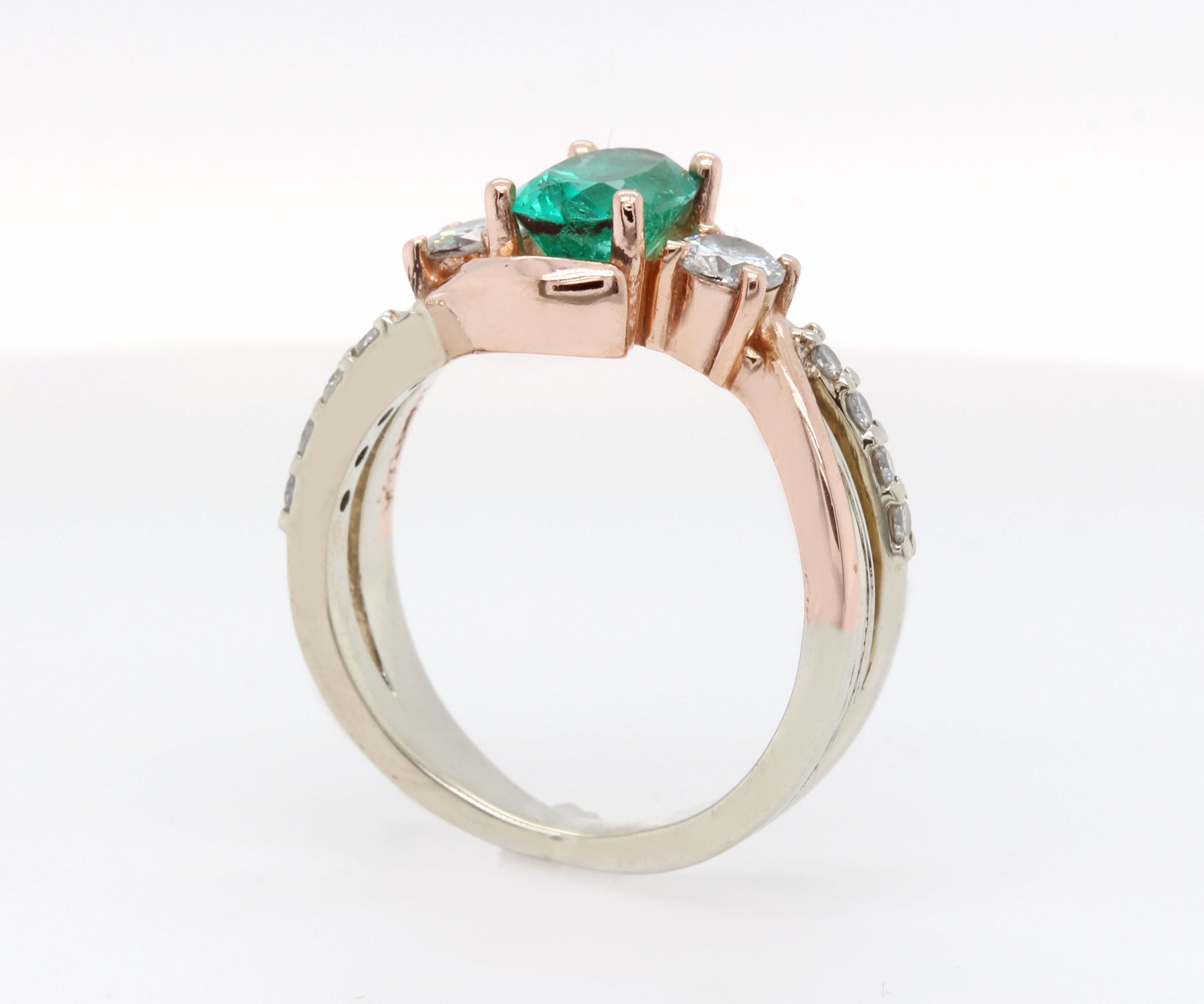 Anillo de oro rosa curvado con diamantes y tres piedras esmeralda